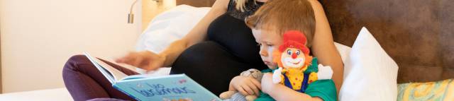 Mother lies in bed with son and reads a book