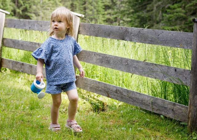 Little girl runs along a fence in a meadow with a watering can