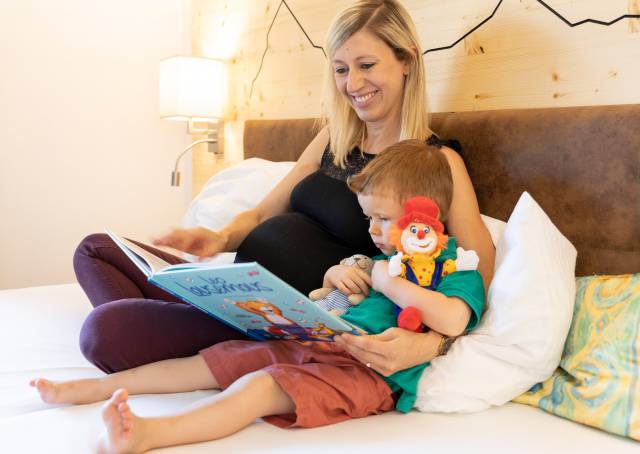 Mother lies in bed with son and reads a book