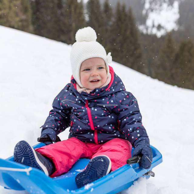 Child sitting on a sledge in the snow in Tyrol