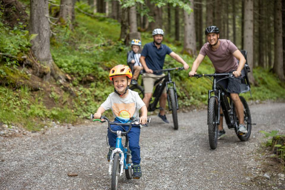 Fathers with children mountain biking through the forest in Berwang