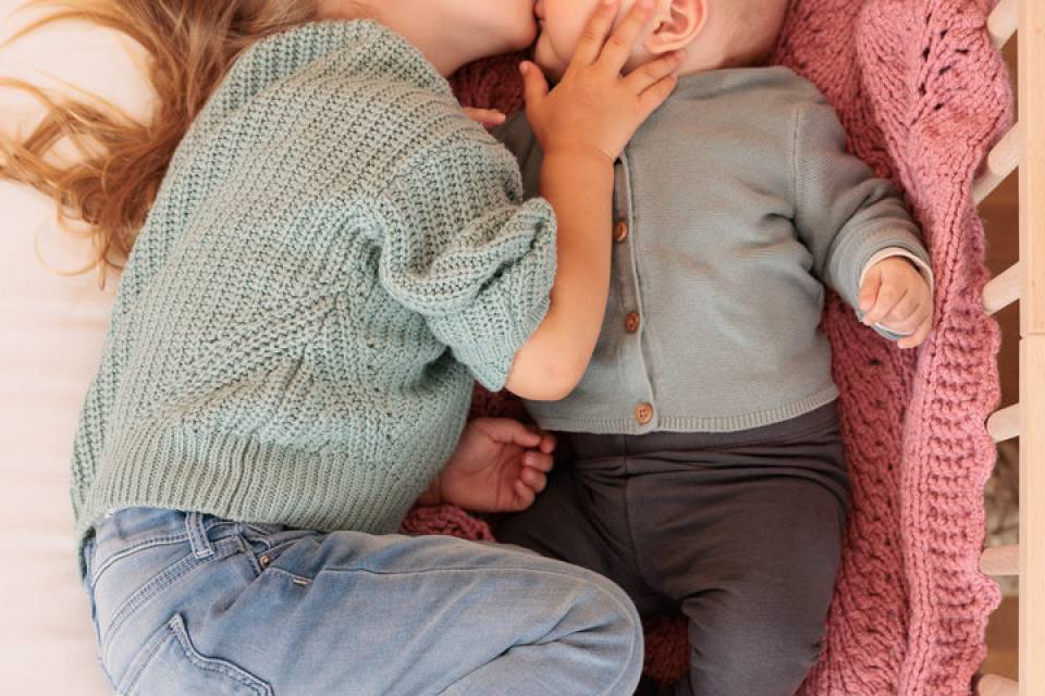 Die größere Schwester gibt dem Baby ein Kuss auf die Nasenspitze